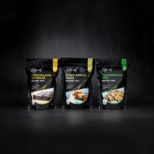 Lots of Baking Mixes Chocolate Crunch, Spicy Apple Cake and Gingerbread Men baking mixes in black packaging on a dark background.